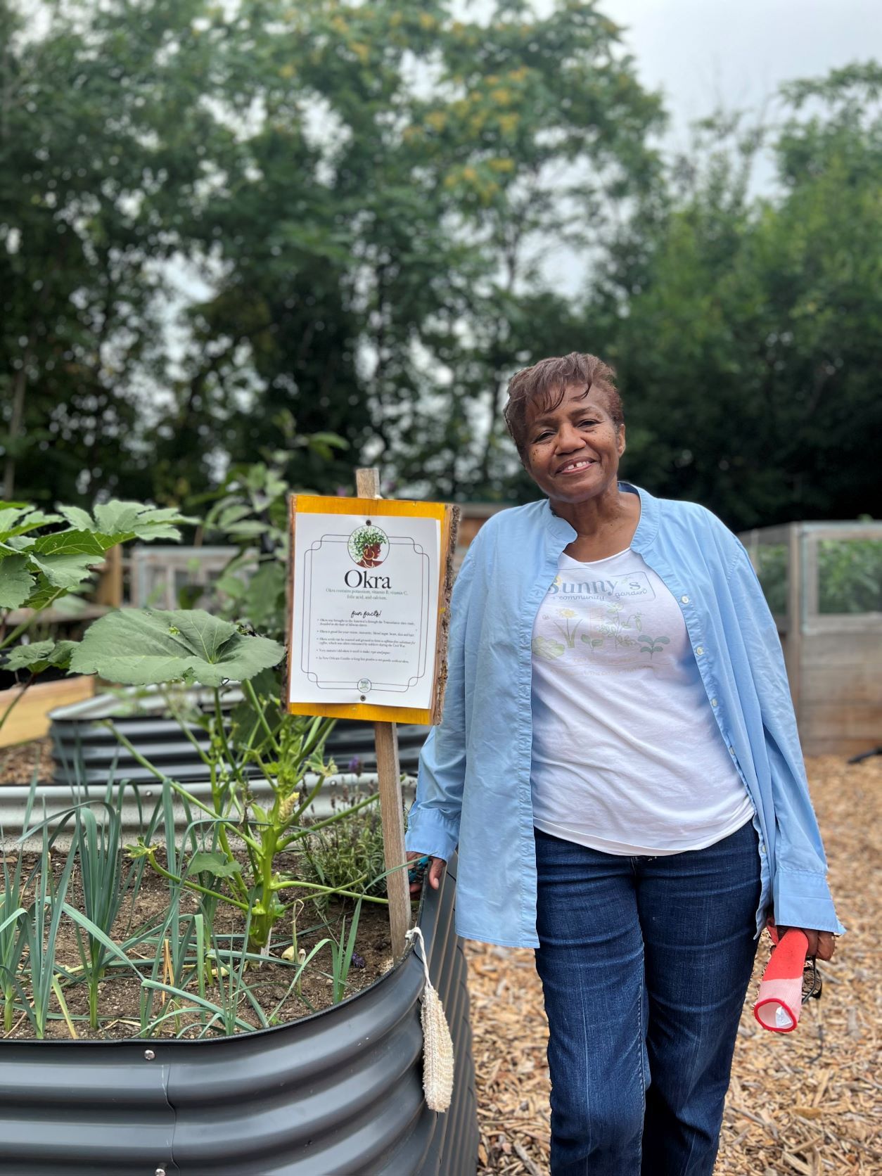 Sheila Petite standing next to an Okra raised garden bed at Sunny's community garden.