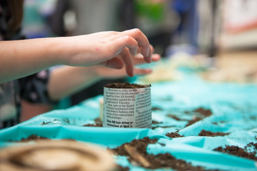 An ESY student plants seeds in a newspaper pot. 